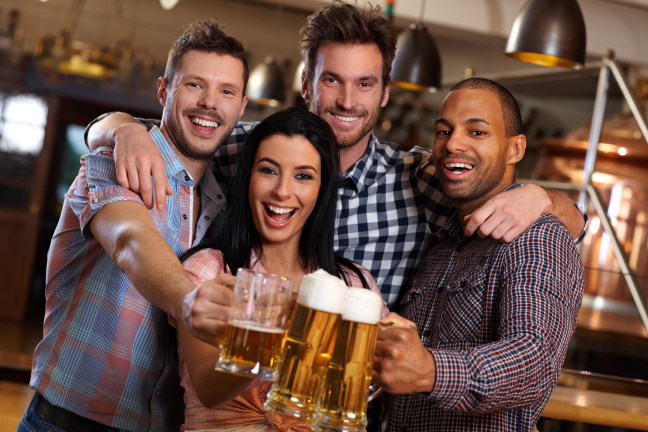 Group of happy young friends drinking beer at pub, laughing, clinking glasses